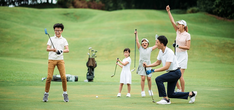 A family of five, playing golf, celebrating one of the children making a hole in one putt. 